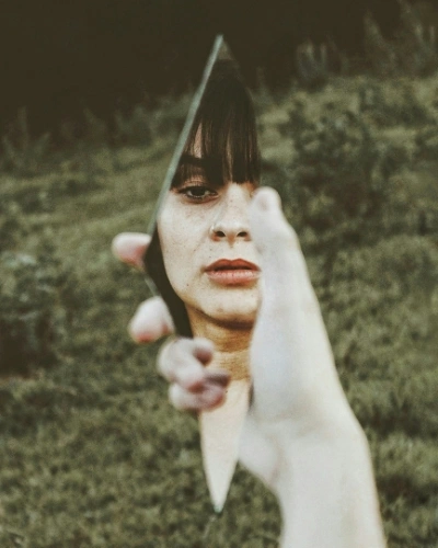 Woman holding a shard of broken mirror looking at reflection
