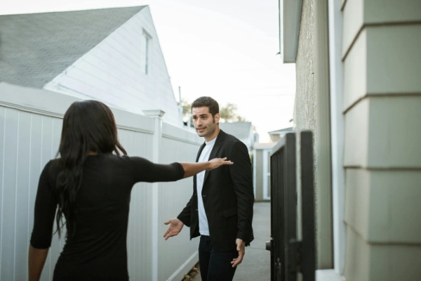 Woman keeping man at arms length outside a house