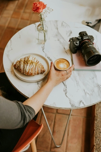 Woman sitting at table with coffee, croissant, and camera