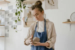 lady in bright room shaping a lump of clay