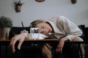 young women resting her head on her shoulder while slouching on a table with a blank look on her face