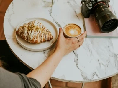 Woman sitting at table with coffee, croissant, and camera