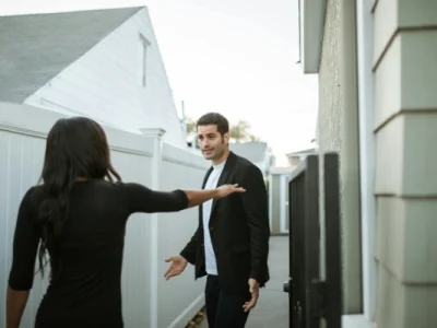 Woman keeping man at arms length outside a house